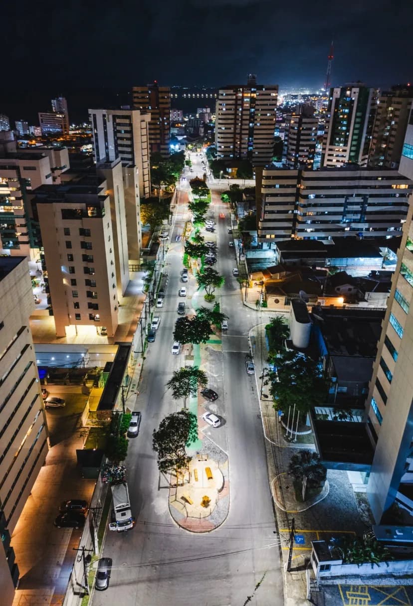 Avenida arborizada vista do alto à noite, cercada por edifícios residenciais iluminados
